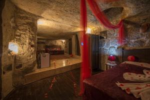 um quarto numa caverna com uma cama e cortinas vermelhas em Cappadocia Antique Gelveri Cave Hotel em Guzelyurt