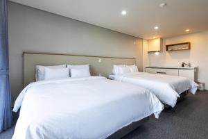 two beds in a hotel room with white sheets at Aewol Stay in Jeju Hotel&Resort in Jeju