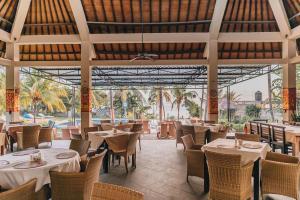 un restaurante con mesas y sillas blancas y palmeras en Ocean View Tulamben Dive & Resort, en Tulamben