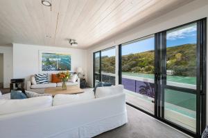 Kawau Lodge Boutique Resort في Kawau Island: غرفة معيشة بأثاث أبيض ونوافذ كبيرة