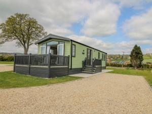 a green tiny house with a large deck at Hares Meadow in Caersws
