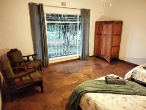 a bedroom with a bed and a chair and a window at Doornspruit Farm in Magaliesburg