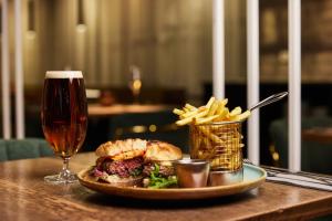 a plate with a sandwich and french fries and a glass of beer at Konvin Hotel by Reykjavik Keflavik Airport in Keflavík
