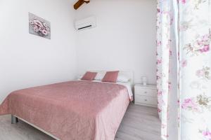 a white bedroom with a pink bed and a curtain at La Terza in Krk