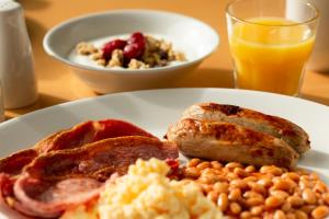 a plate of breakfast food with eggs bacon beans and a glass of orange juice at Holiday Inn Express Earls Court, an IHG Hotel in London