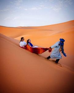 a man pulling two women on a camel in the desert at Sahara Desert Experience camp in Merzouga