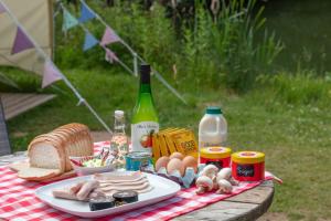 a picnic table with a plate of food and a bottle of wine at Lloyds Meadow Glamping in Chester