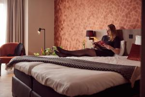 a woman sitting on a bed reading a book at Van der Valk Texel - De Koog in De Koog