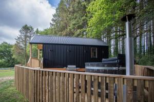 a black building with a fence in a yard at Cabin In The Woods - 1 Bedroom Lodge - Kilgetty in Stepaside