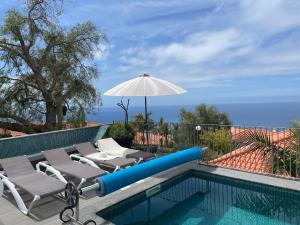 uma piscina com duas espreguiçadeiras e um guarda-sol em Vila Inês - Beautiful 2 bedroom villa with private pool and stunning views of the Atlantic Ocean em Arco da Calheta