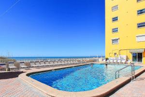 a swimming pool next to a yellow building and the ocean at Holiday Villas III 505 in Clearwater Beach