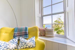 a yellow chair sitting next to a window with pillows at Primrose Cottage in St Ives