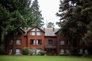 uma grande casa de tijolos com árvores em frente em Rincón de los Andes Resort em San Martín de los Andes