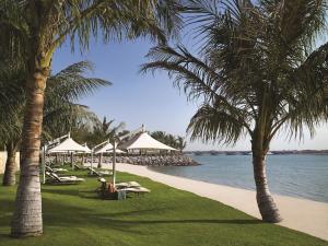 una playa con palmeras, sillas y sombrillas en Shangri-La Hotel Apartments Qaryat Al Beri, en Abu Dabi