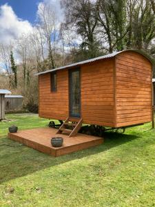 a wooden cabin with a deck in the grass at Swaledale Shepherd's Hut in Newton Abbot