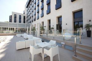 un patio con sillas blancas y una mesa y un edificio en M.A. Hotel Sevilla Congresos, en Sevilla