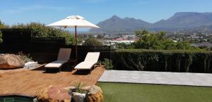 a wooden deck with two chairs and an umbrella at African Violet Guest Suites in Noordhoek