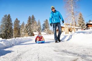 Ein Mann, der ein Kind auf einem Schlitten auf einer schneebedeckten Straße zieht in der Unterkunft Reka-Feriendorf Montfaucon in Montfaucon
