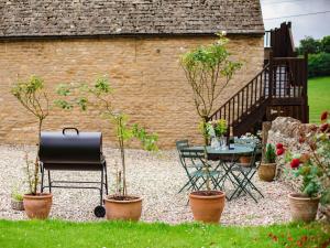 a garden with a table and chairs and potted trees at Hayloft at NewBarn Farm in Chipping Norton