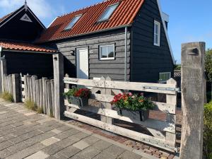 a black house with a wooden fence and flowers at Dijkhofje, dichtbij strand, zee en meer. in Vrouwenpolder