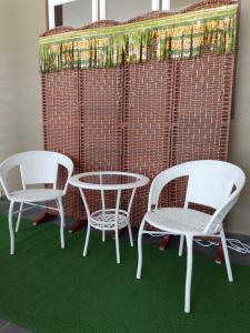 drie witte stoelen en een tafel en een muur met groen tapijt bij Homestay Qaseh Kerteh in Kerteh