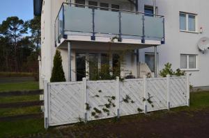 a white fence in front of a house with a balcony at Ferienwohnung Maigloeckchen 05 str in Karlshagen