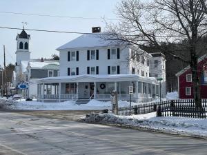 Cornish的住宿－The Cornish Inn，白雪 ⁇ 的街道上一座白色的建筑,上面有钟楼