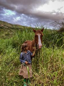 una niñita parada junto a un caballo marrón en un campo en Hotel Fundo Achamaqui, en Chachapoyas