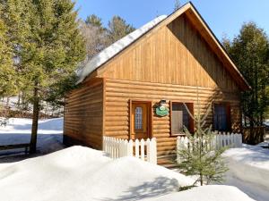una cabaña de madera en la nieve con una valla blanca en La Sapinette en Val-David