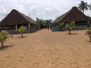 a sandy beach with two huts and palm trees at Villa Cocotiers A11 in Cotonou