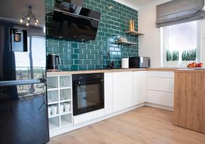 a kitchen with white cabinets and green tiles at Luxus Apartament Tulipan in Gdynia