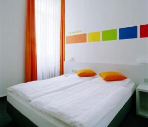 a white bed with two orange pillows on it at Colour Hotel in Frankfurt/Main