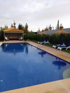 a large blue swimming pool with chairs and a gazebo at Villa famille Bilal Agafay in Marrakesh