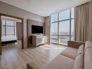 Movenpick Jumeirah Village Triangle في دبي: غرفة معيشة بها أريكة وتلفزيون