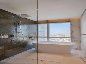 een badkamer met een bad en een douche met een raam bij Movenpick Jumeirah Village Triangle in Dubai