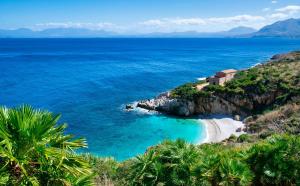 una spiaggia con una casa su una collina vicino all'oceano di Akoya Apartments a San Vito lo Capo