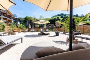 a patio with tables and chairs and an umbrella at Wellness und Brunch Hotel MorgenZeit beheizter Naturpool mit Sandstrand Genuss Frühstück bis 13 Uhr Hochkönig Sommercard in Maria Alm am Steinernen Meer