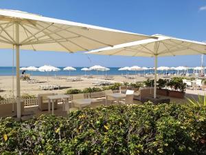 a beach with tables and umbrellas and the ocean at Hotel Miramare in Castiglione della Pescaia
