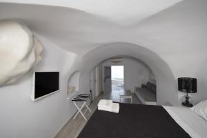 a white living room with a couch and a tv at Anemos Cave Suites in Imerovigli