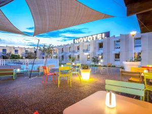 リヴサルトにあるNovotel Perpignan Nord Rivesaltesのホテル正面のパティオ(カラフルなテーブルと椅子付)