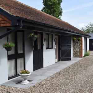 a white building with a black door and flower pots on it at Sandhurst Farm Forge Self Catering Stableblock in Sittingbourne