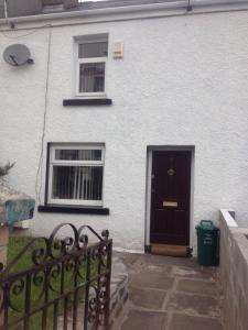 a white house with a black door and a fence at Honeycomb Cottage in Aberdare