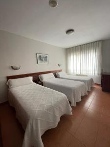 Habitación con 4 camas con sábanas blancas. en Hotel Valdés, en Gijón