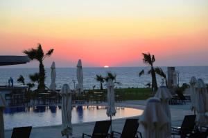 a resort pool with chairs and umbrellas at sunset at Amphora Hotel & Suites in Paphos