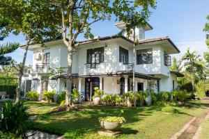 Una casa blanca con un árbol delante. en Villa Sarakkuwa, en Pamunugama