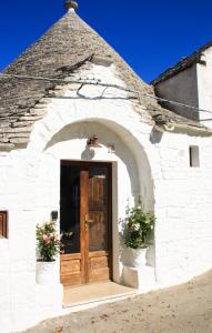 a white building with a wooden door and two potted plants at EnjoyTrulli - Unesco Site in Alberobello
