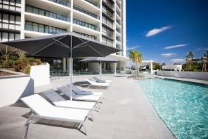 una piscina con tumbonas y una sombrilla junto a un edificio en Mantra Sierra Grand, en Gold Coast