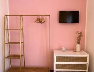 a room with a pink wall with a shelf and a tv at Miss Scola Pastry Rooms - Lake Como in Abbadia Lariana
