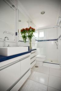 a white bathroom with a sink and a vase of red flowers at Apartamento Triplex Place Vendome in Sao Paulo
