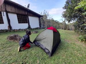a person kneeling on the grass next to a tent at Gran Camping Cabanas da Fazenda in Visconde De Maua